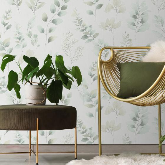 Fashion for Walls - Moments26 romantischer Wohnbereich, Tapete Blättermuster in sanften Grüntönen, Rattan Sessel mit Kissen und grünem Beistelltisch.