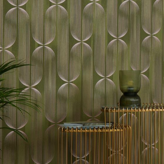 Elle Decoration 5 Vliestapete mit geometrischem Retro-Muster in Olivgrün und zarten Rosé-Metallic Akzenten – stilvoller Wohnbereich kombiniert mit goldfarbenen Konsolentischen und üppiger Grünpflanze. - Elle Decoration 5