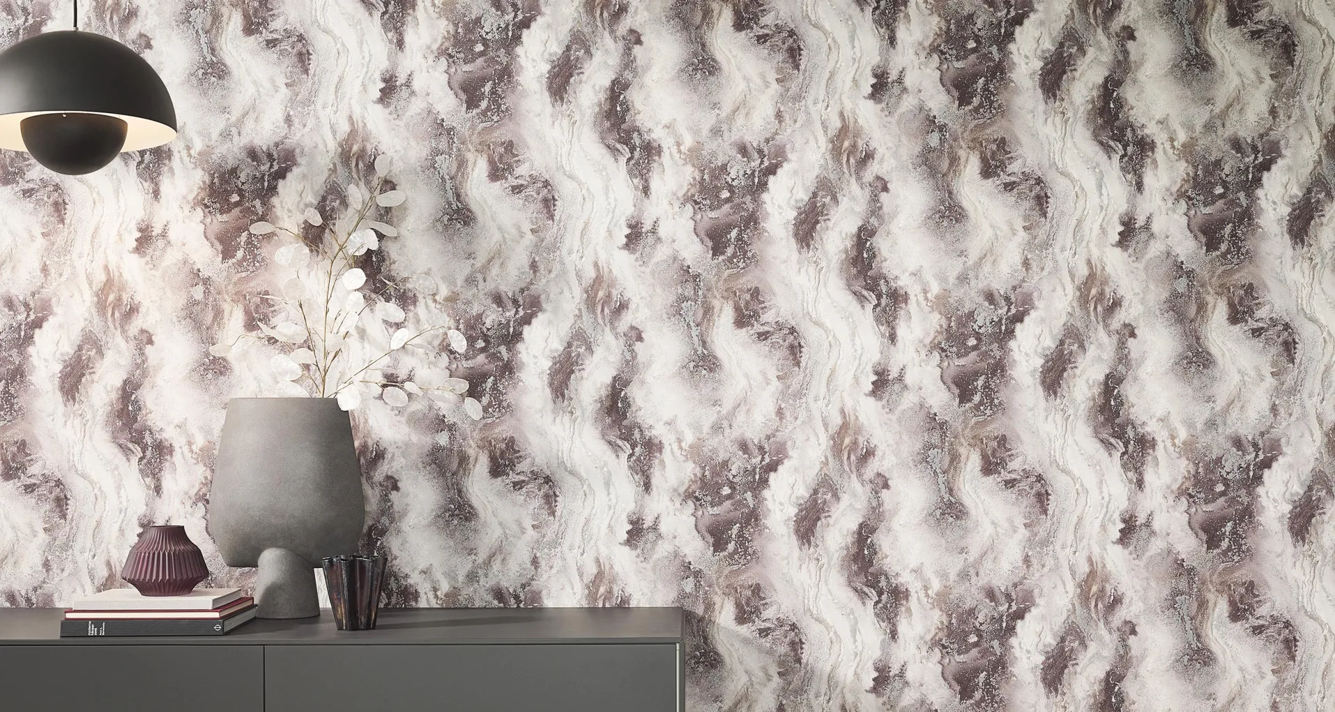 Elle Decoration 5 Vliestapete mit fließender Marmoroptik in Creme-, und Violetttönen – eleganter Wohnbereich kombiniert mit dunklem Sideboard und modernen Wohnaccessoires.